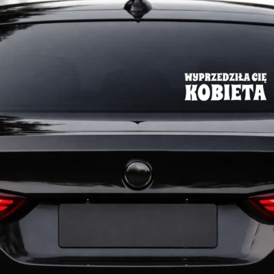 naklejka na samochód z napisem WYPRZEDZIŁA CIĘ KOBIETA biała folia na szybę